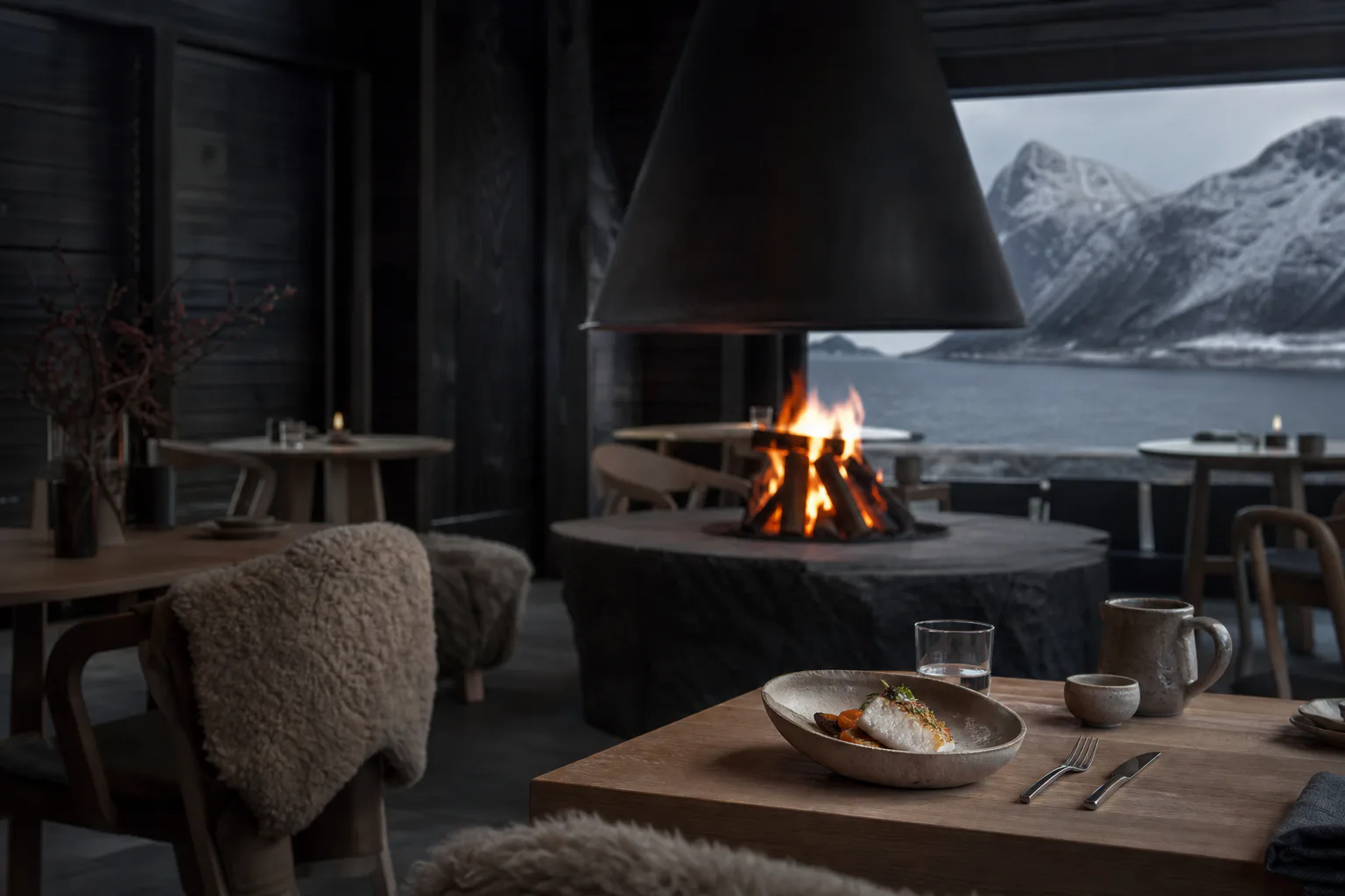 The dining room at Fyr facing the fjord through full-height glass with a fire lit at one end.